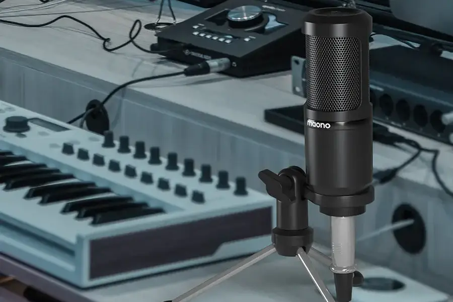 A microphone on a tripod in front of a keyboard and computer setup for recording purpose.